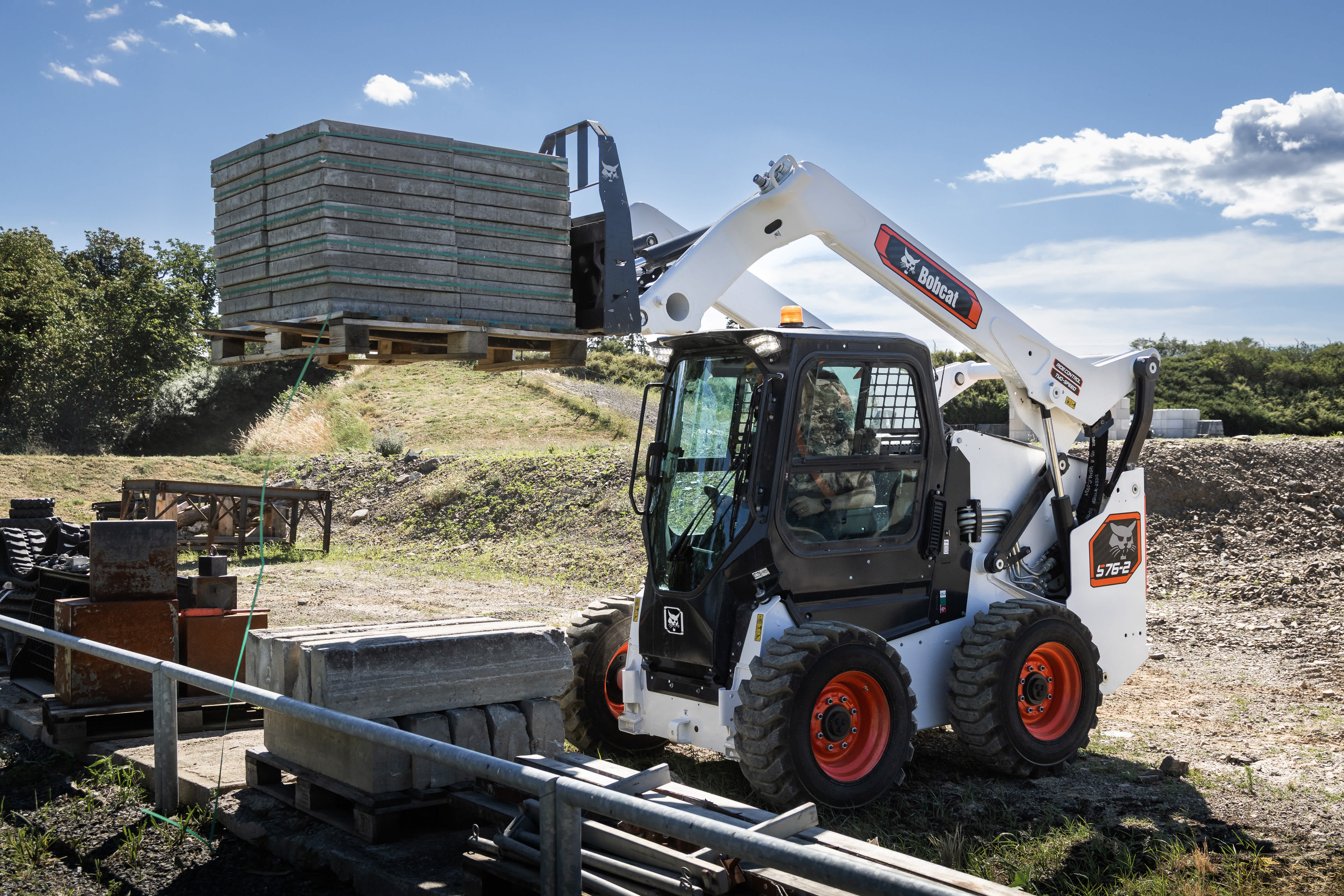 Bobcat Pro S76-2 Skid-Steer Loader with Pallet Fork Attachment Lifting a Stack of Concrete Slabs at a Construction Site