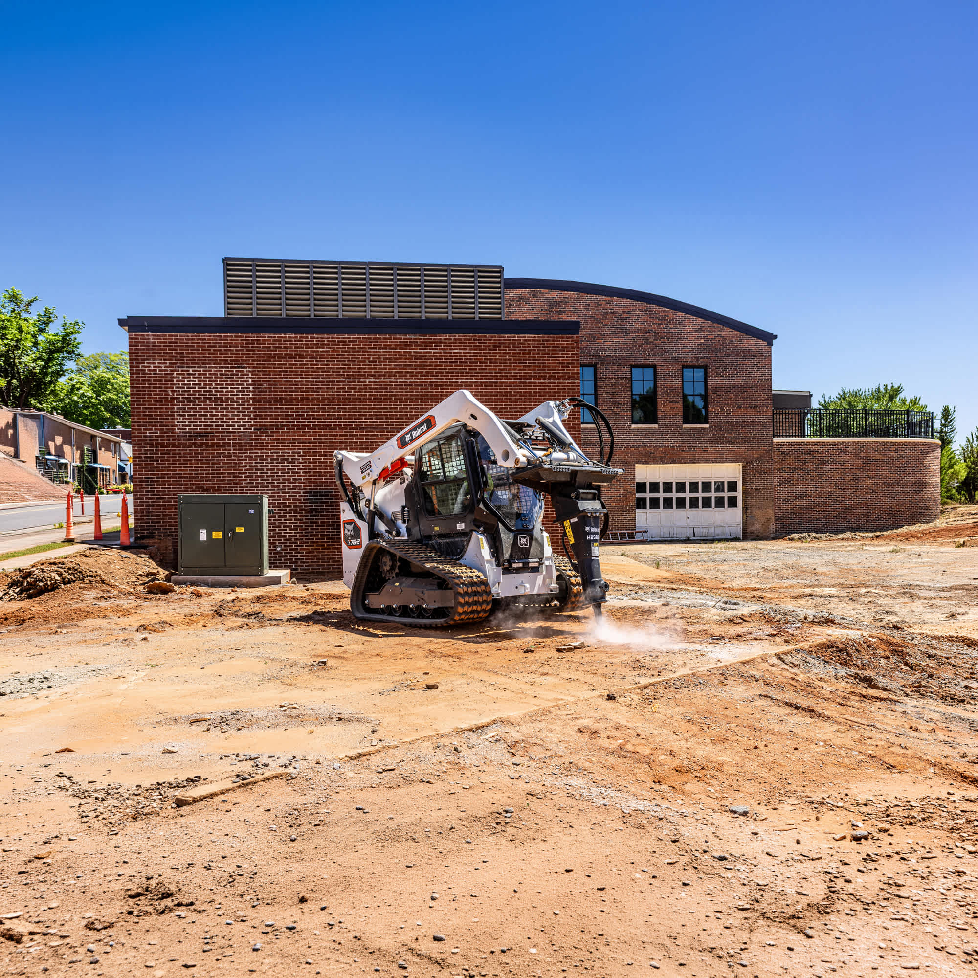Front right quarter view of an operator demolishing concrete with a breaker attached to a Bobcat T76-2 Pro Compact Track Loader at a commercial construction site