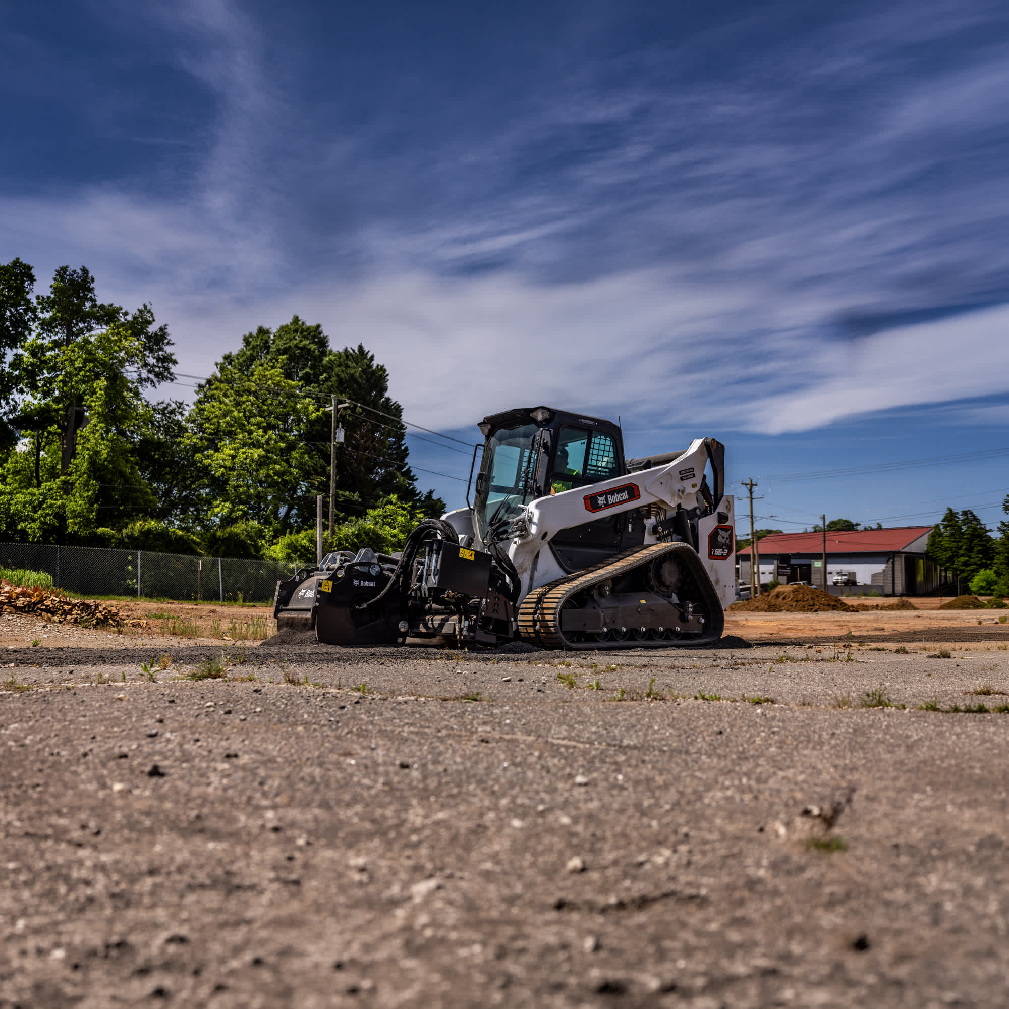 Left side view of an operator spreading asphalt at a commercial construction site using a 24" high flow planer attached to a Bobcat T86-2 Pro Compact Track Loader
