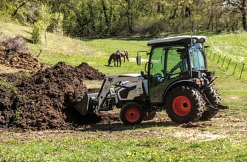 Operator Using Bobcat Compact Tractor With Front-End Loader To Lift Dirt From Pile In Field