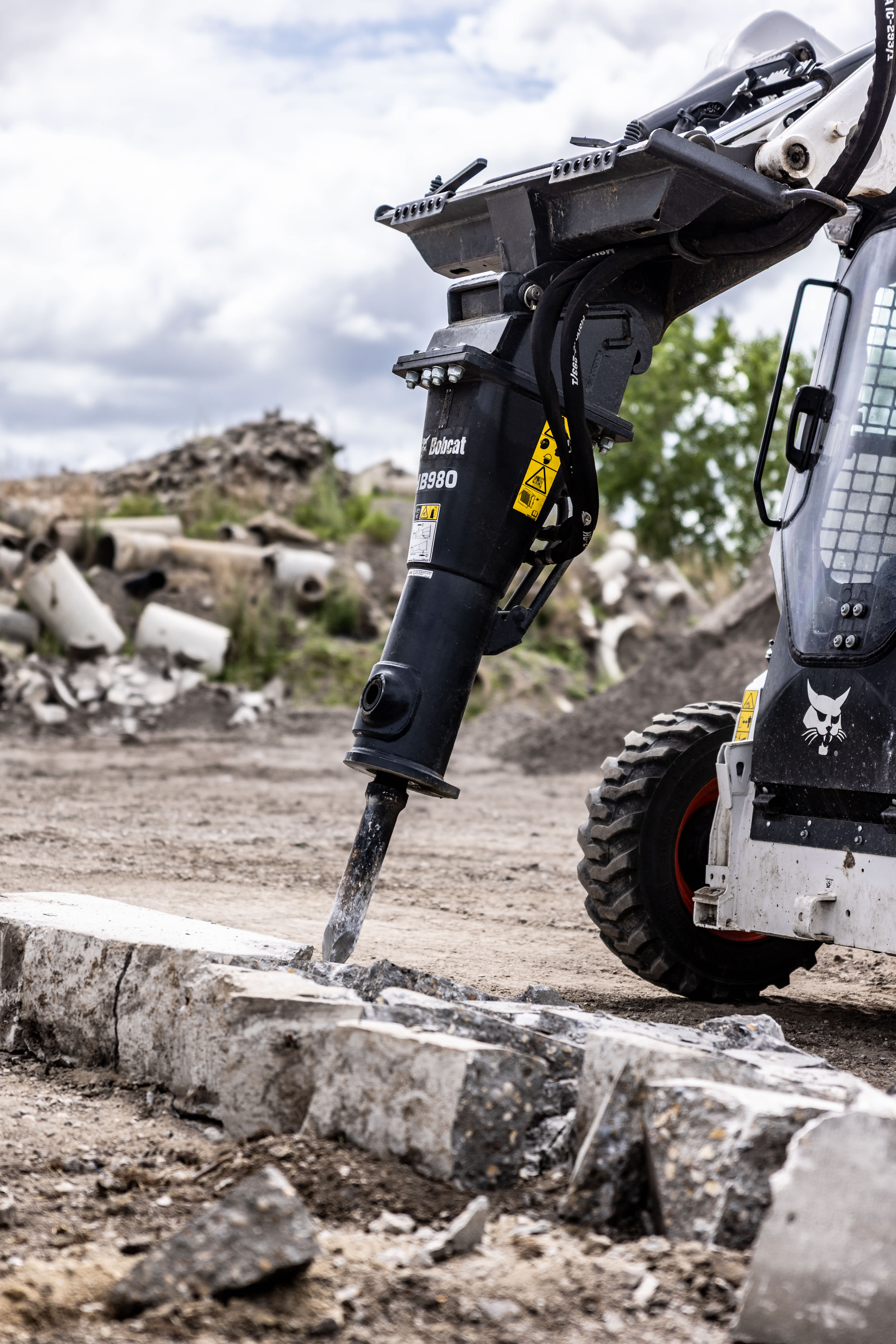 Bobcat HB980 hydraulic breaker attachment on a Bobcat skid-steer loader breaking concrete slab at a jobsite