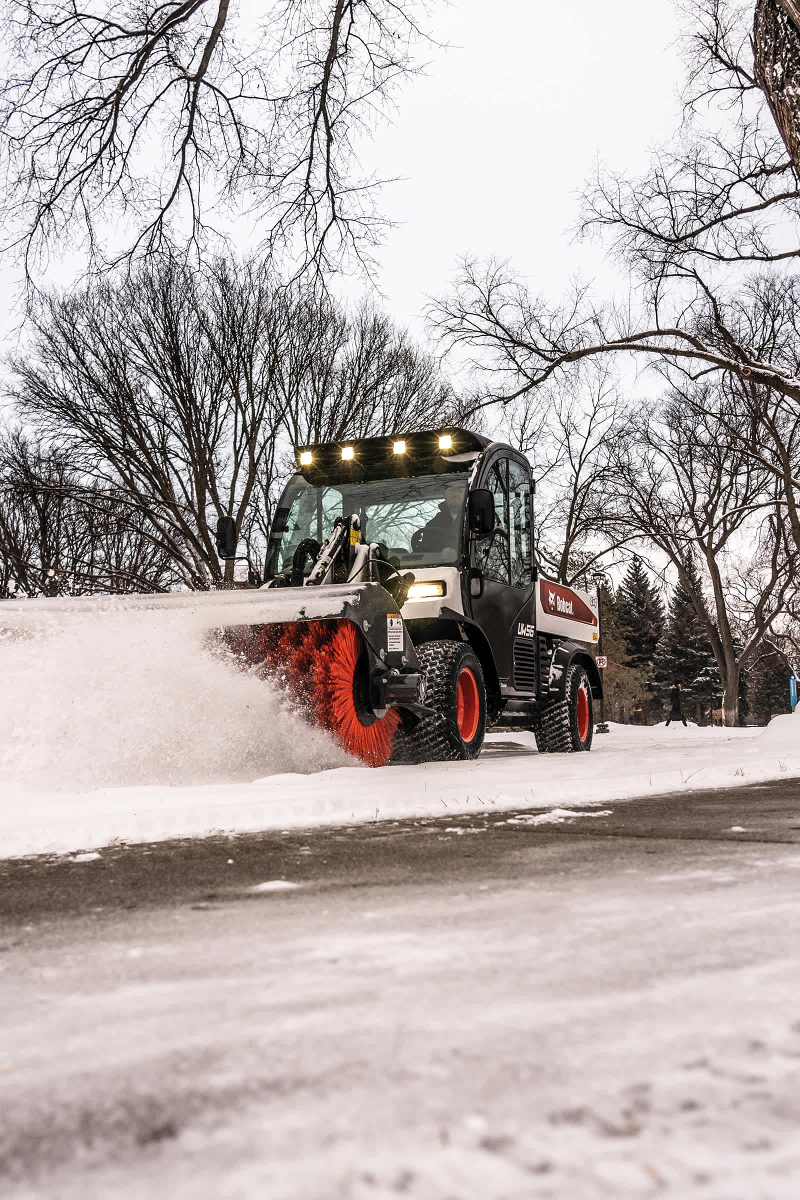 An Operator Uses a Toolcat Utility Work Machine and an Angle Broom Attachment to Move Snow From a Sidewalk