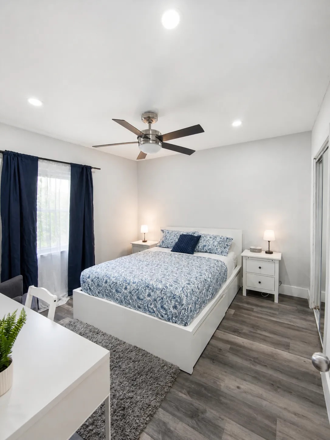 One-bedroom with nightstands, ceiling fan, mirrored closet, and blue-and-white bedding