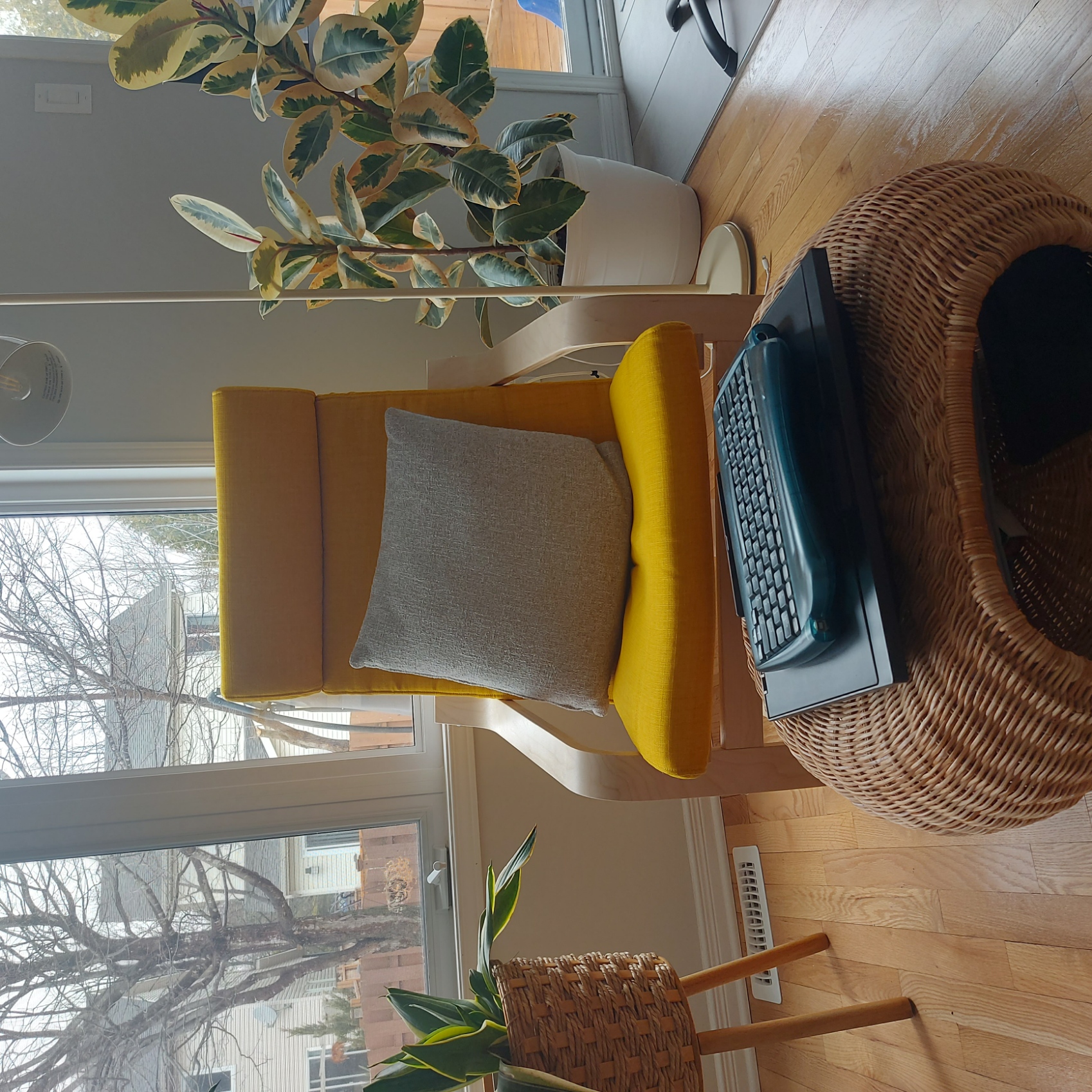A chair and a footstool surrounded by plants and in front of large windows.