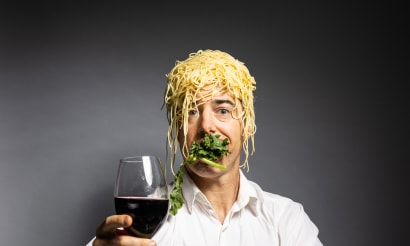Geoff Sobelle holding a glass of wine with food surrounding him