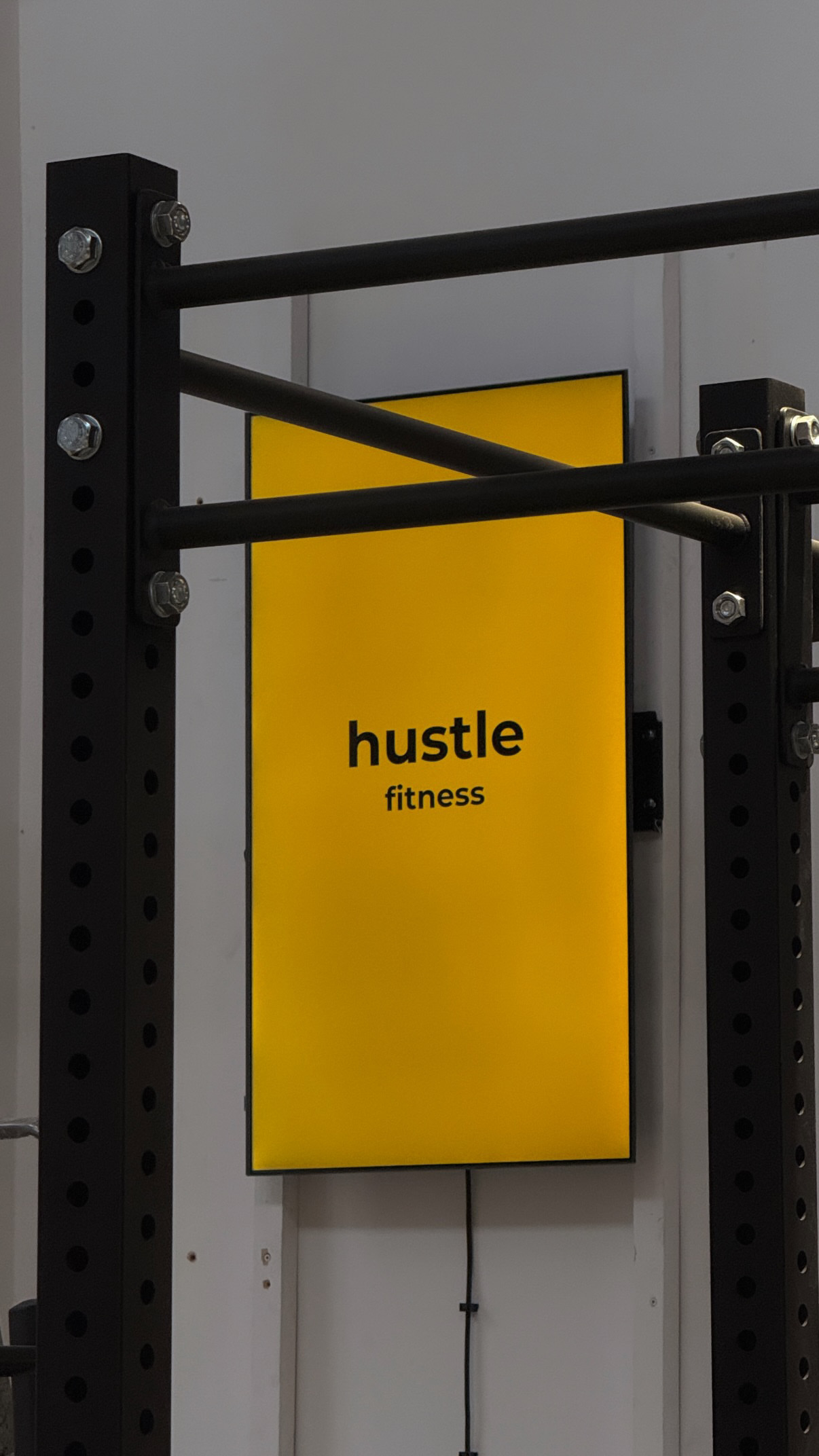 Logo Hustle Fitness na stojaku treningowym