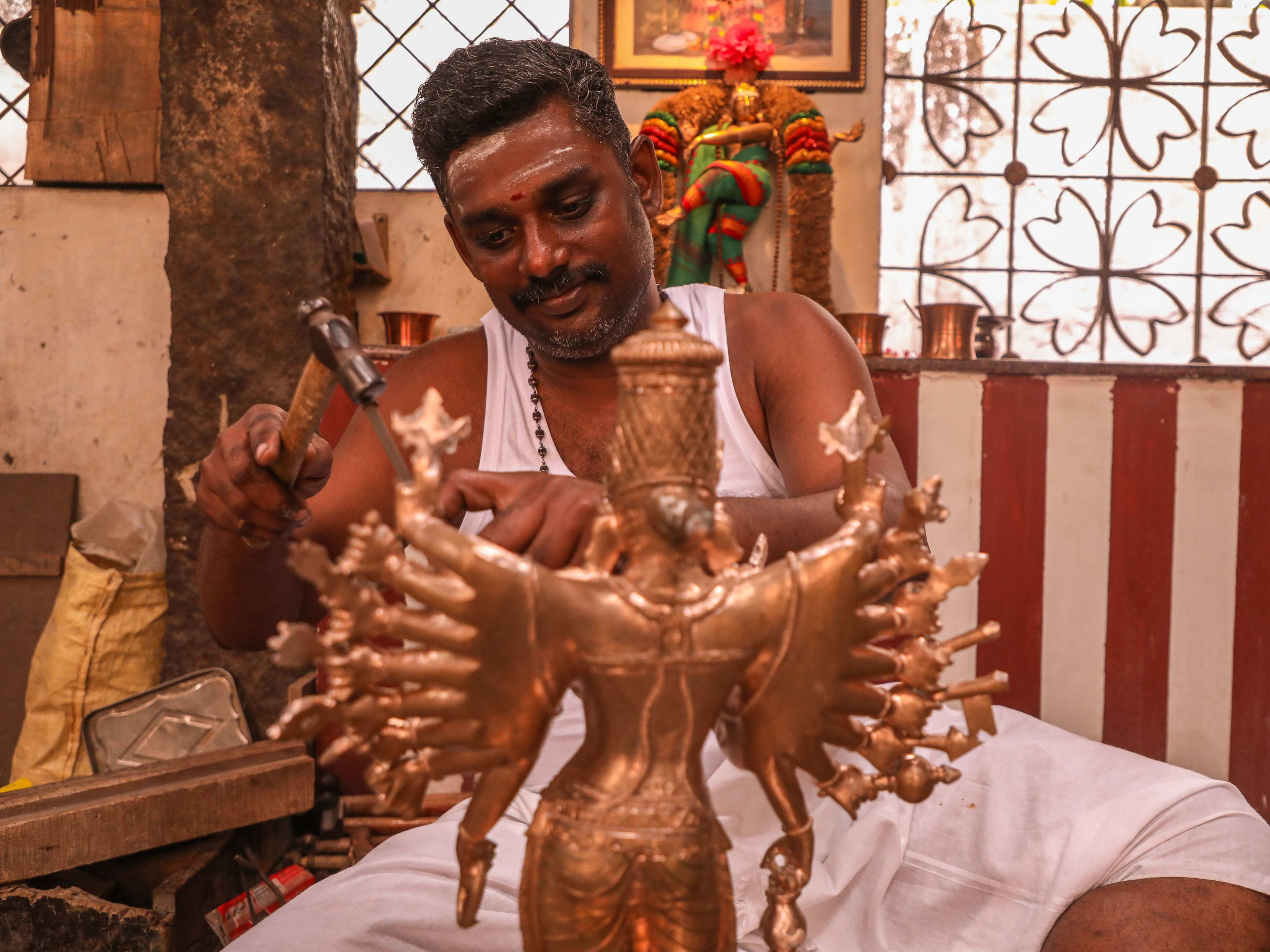 An artisan shaping a brass deity figure by hand