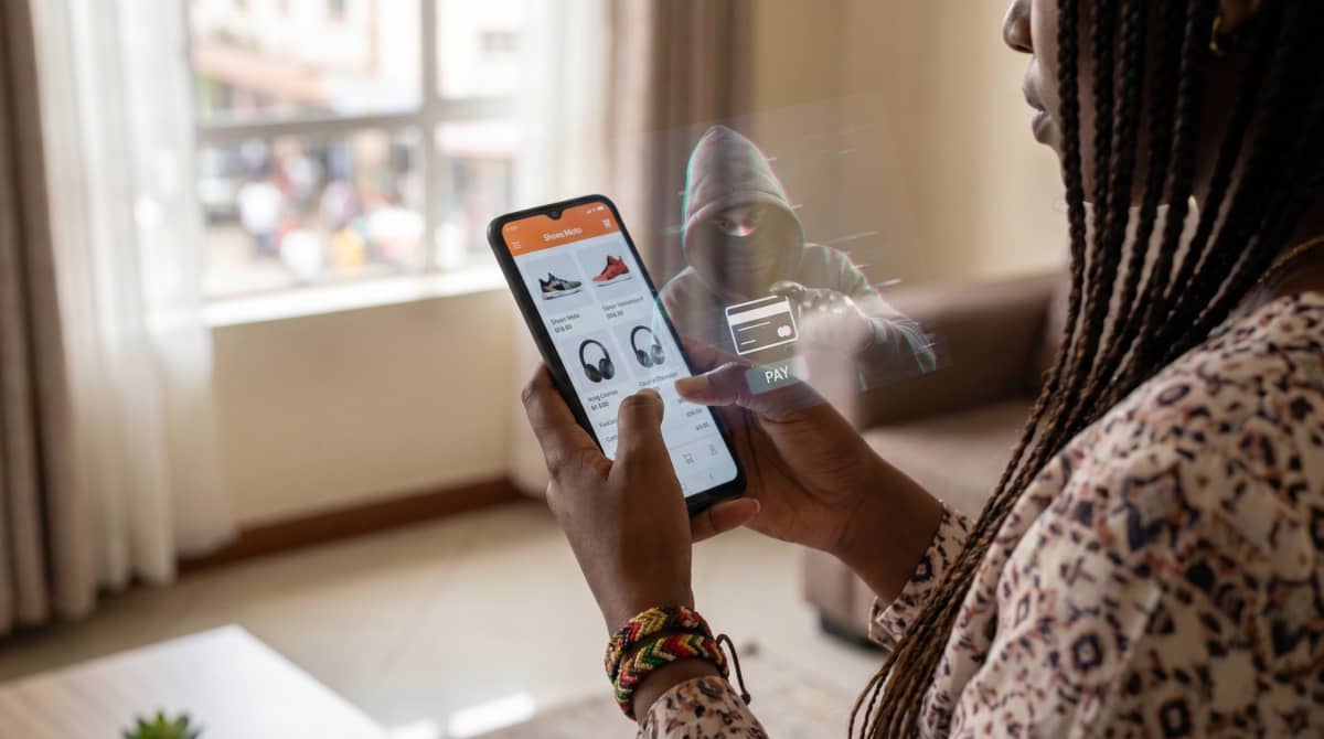 Photo of a person using their phone while a scammer is watching