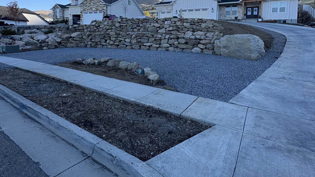 Curved boulder retaining wall with a fresh gravel bed between new concrete curb and driveway
