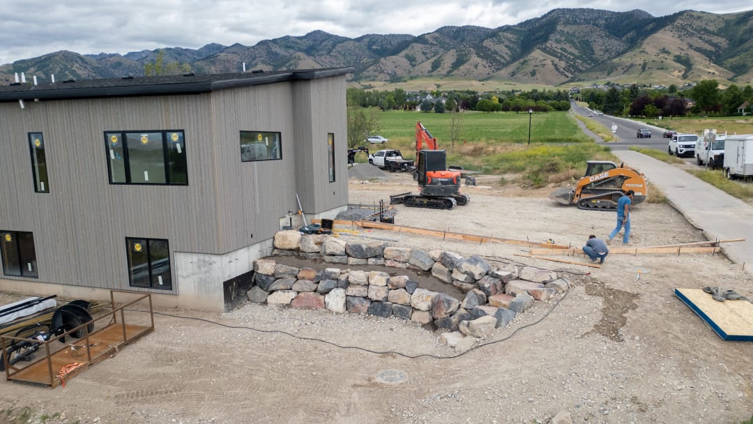 Boulder wall courses being set in an open cut beside a new building, machines on site