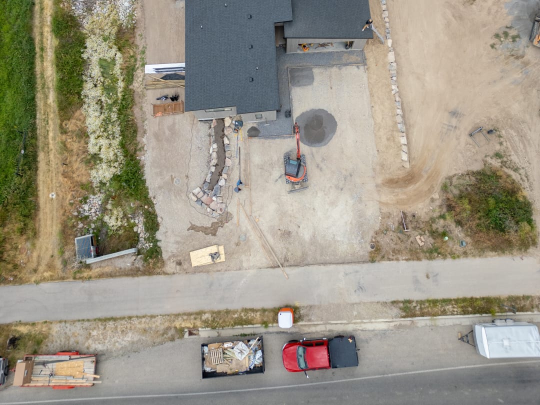 Overhead drone view of a home site with rock walls set, pads graded, and paths cut in