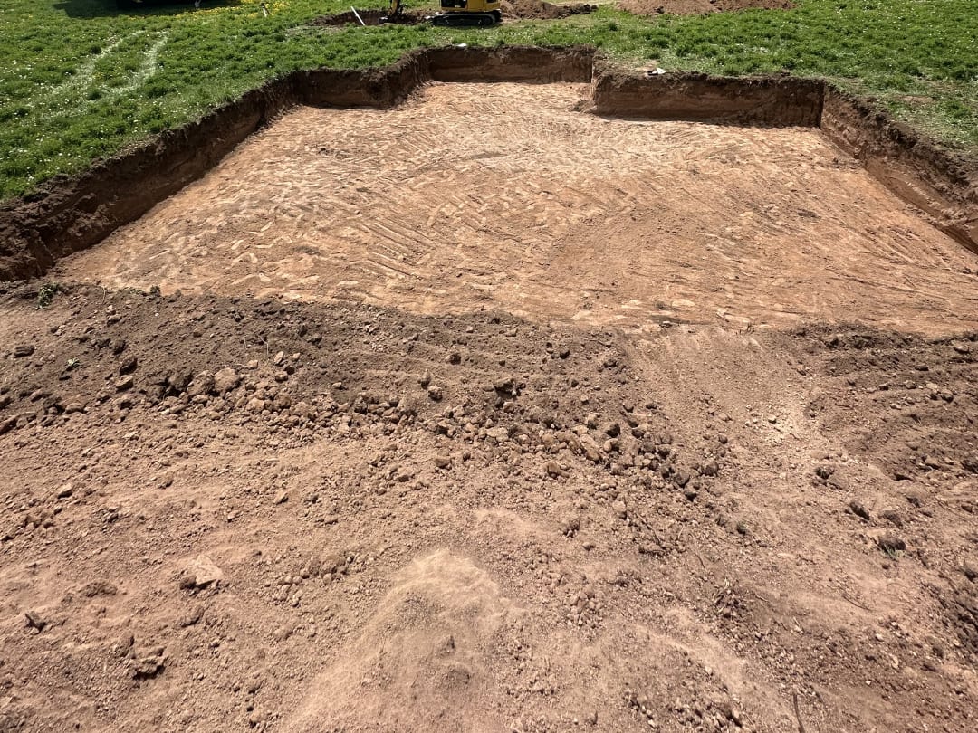 Cabin pad cut and leveled in a mountain meadow, mini excavator working behind it