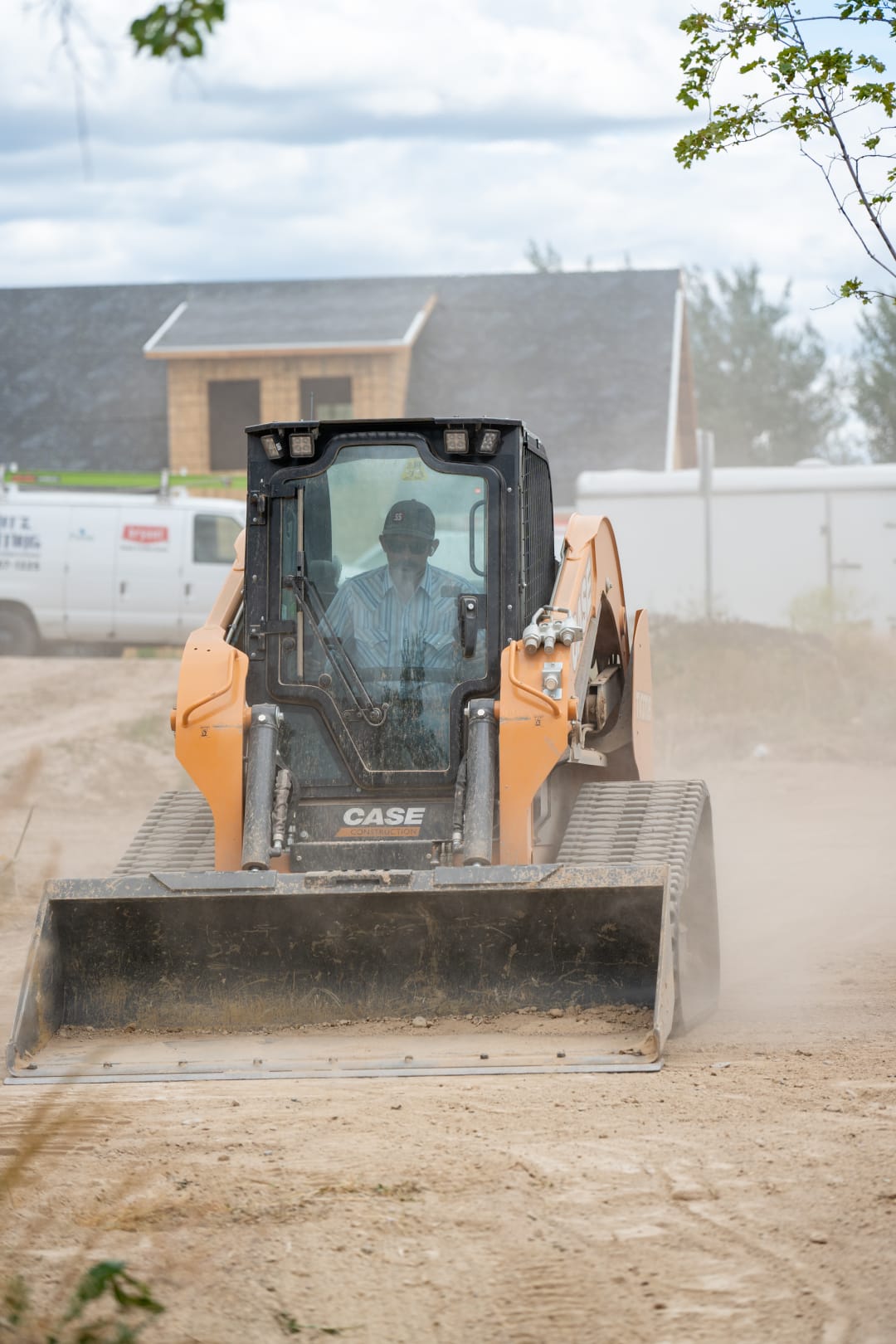 Compact track loader working through dust on a cleared building lot