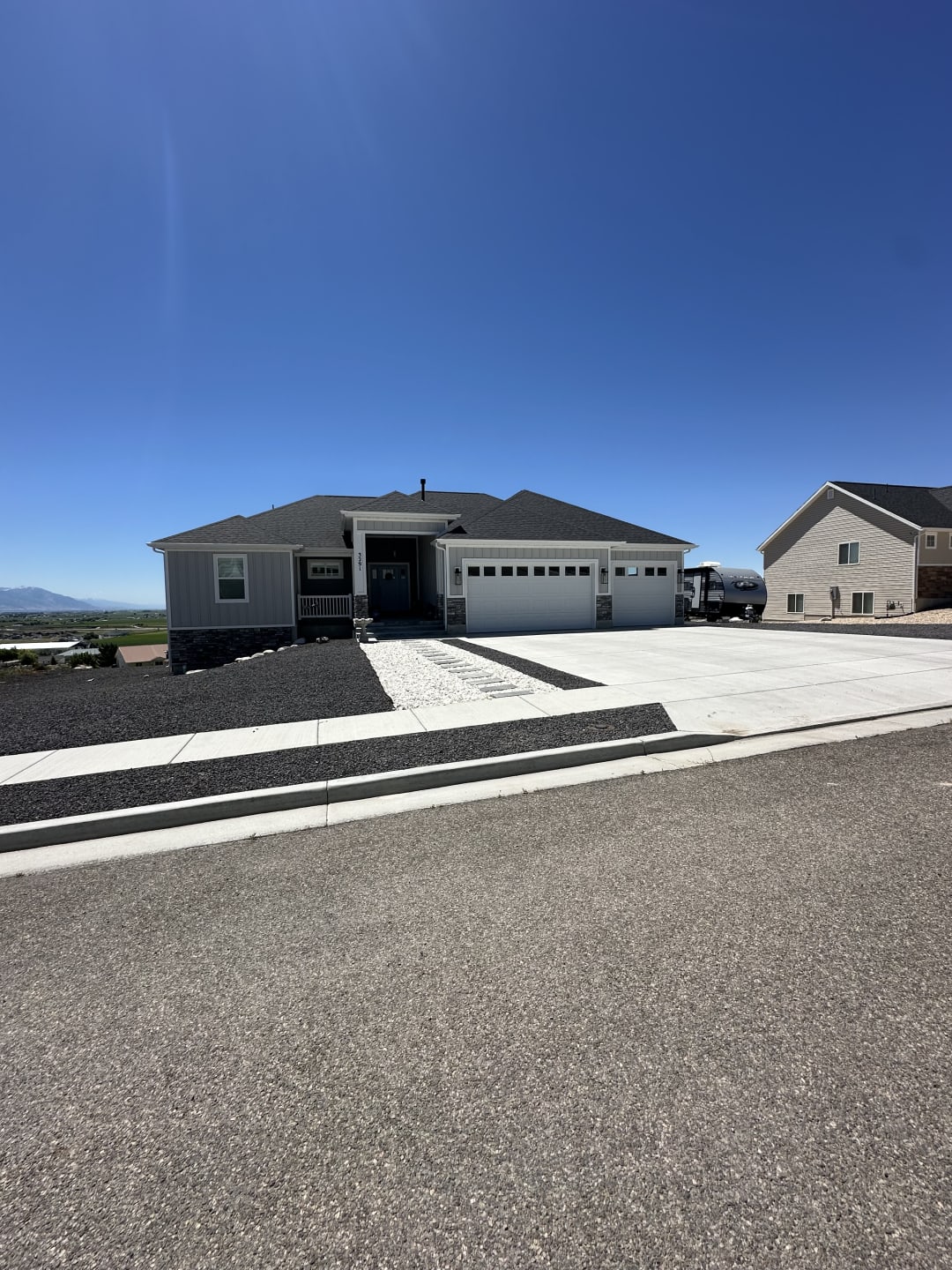 Finished front yard with contrast rock beds, white boulder accents, and a broom-finished concrete driveway