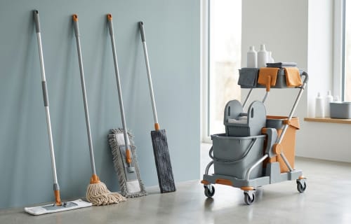 Verschiedene Wischmopps lehnen ordentlich an einer Wand neben einem Reinigungswagen in einem hellen Raum
