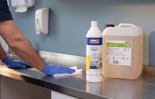 Wischdesinfektion einer Edelstahlfläche, daneben Buzil Budenat Rapid D 444 und ECOLAB Incidin Pro