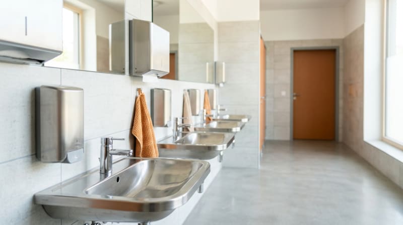 Frisch geputzter heller Sanitärraum einer Schule mit glänzenden Waschbecken und gefüllten Spendern