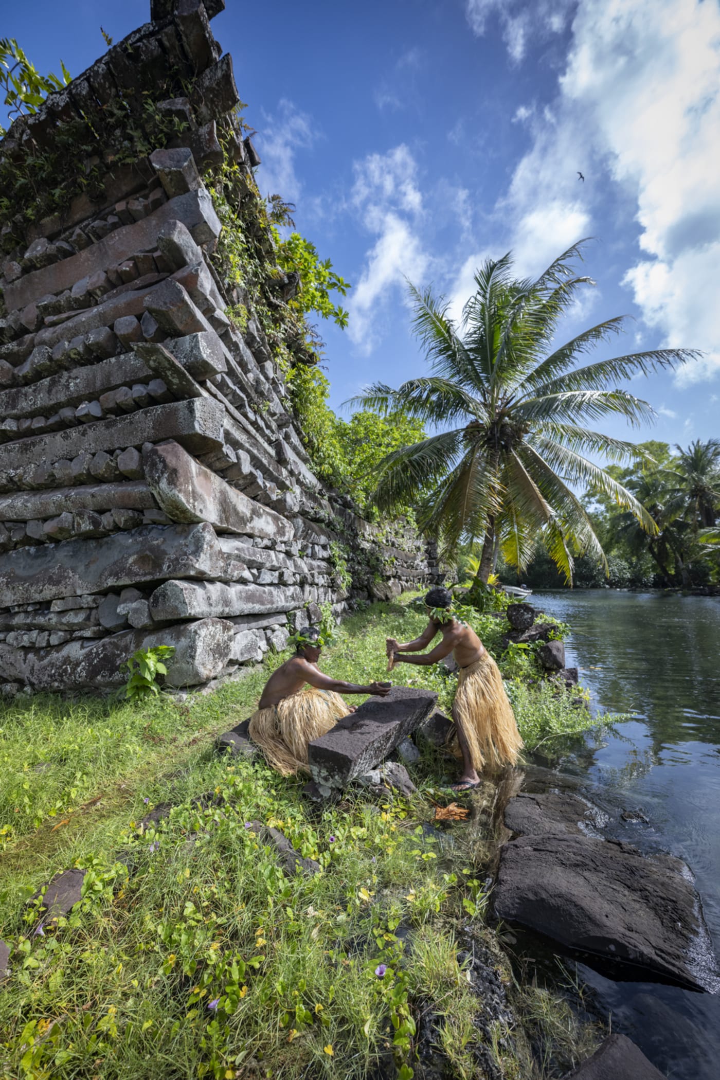 Massive basalt columns stacked into the walls of Nan Madol, with palms and blue sky overhead