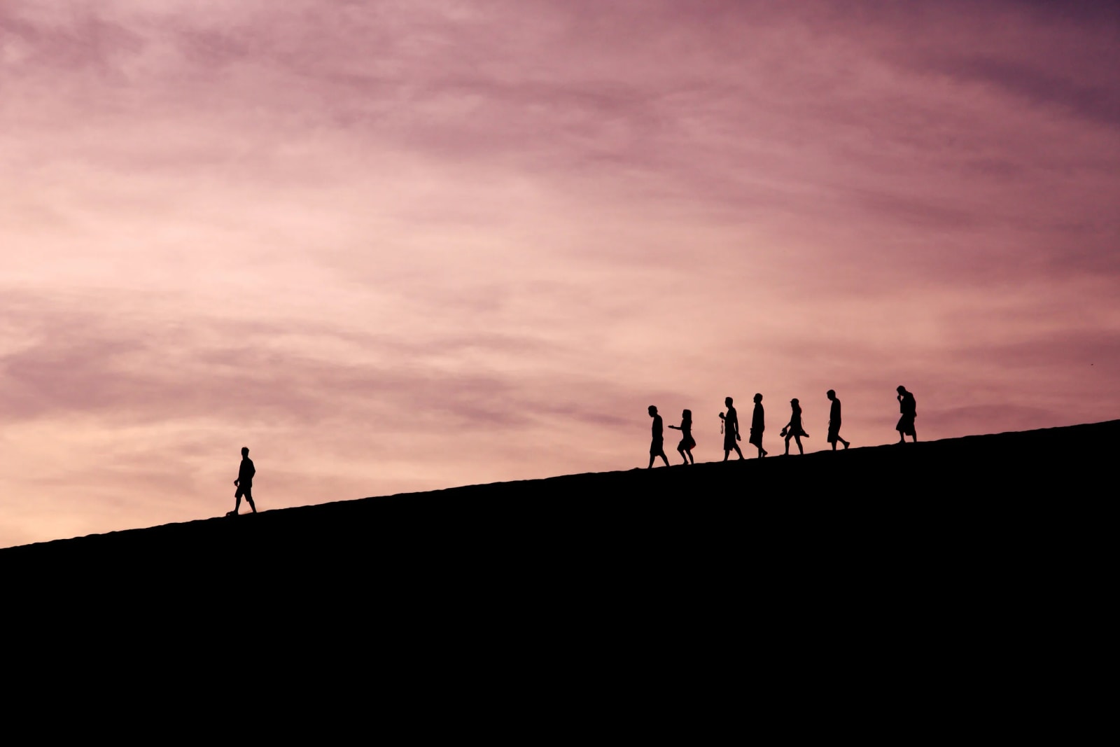 A silhouette of a person standing on a dune with other people in the background at sunset.