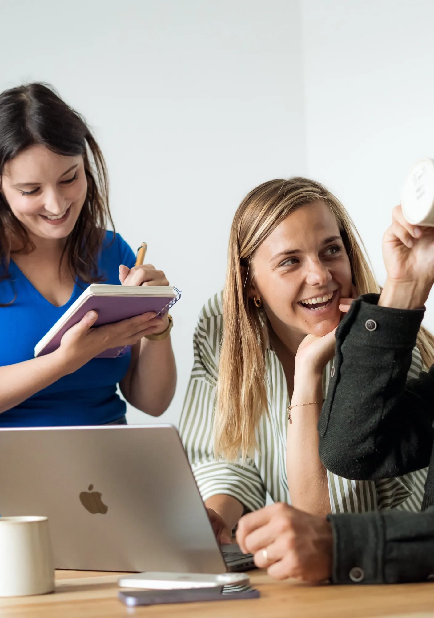 Trois membres de l'équipe souriants autour d'un ordinateur portable, l'une prenant des notes dans un carnet