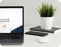 Ordinateur portable ouvert sur un site web, posé sur un bureau blanc à côté d'une plante, d'un smartphone et d'une souris