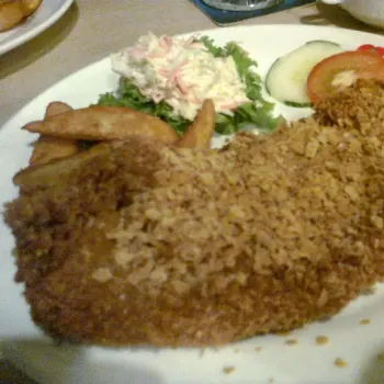 Cereal Fish served on the side with coleslaw, sliced cucumber and tomato and potato wedges