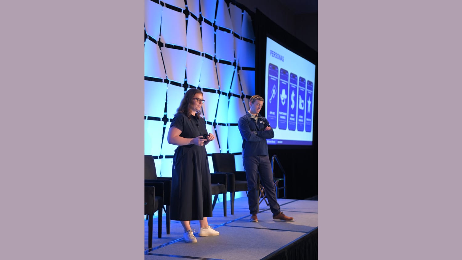 Two people standing on stage at an indoor event.