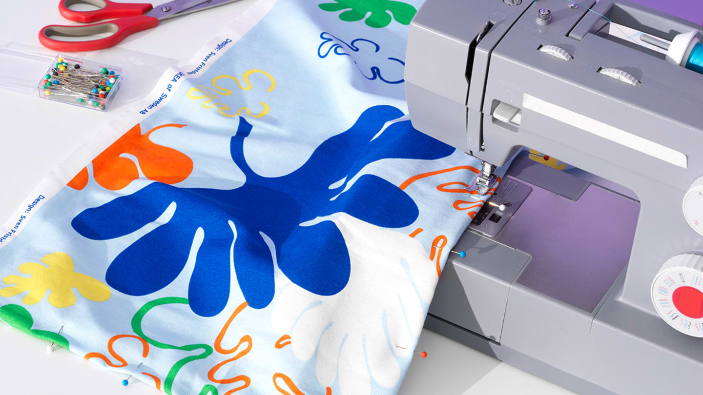 A silver sewing machine with a white cloth with blue and orange floral designs underneath it.