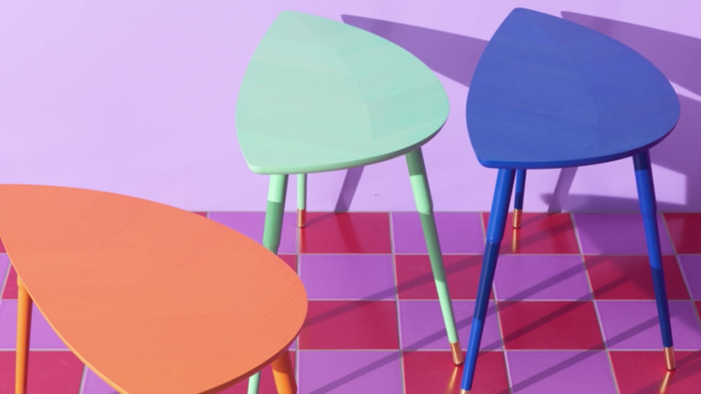 Three triangular tables in orange, light blue, dark blue, placed in a room with light pink walls and light and dark pinked checkered floors.