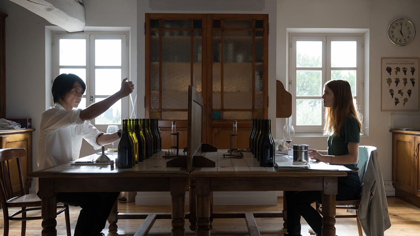A man and a woman sit across from each other at a large table using bottles and droppers placed in front of them.
