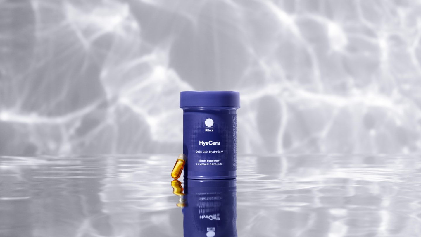 Dark blue cylindrical pot labeled Hya Cera Daily Skin Hydration against a light grey background which seems to reflect a watery background