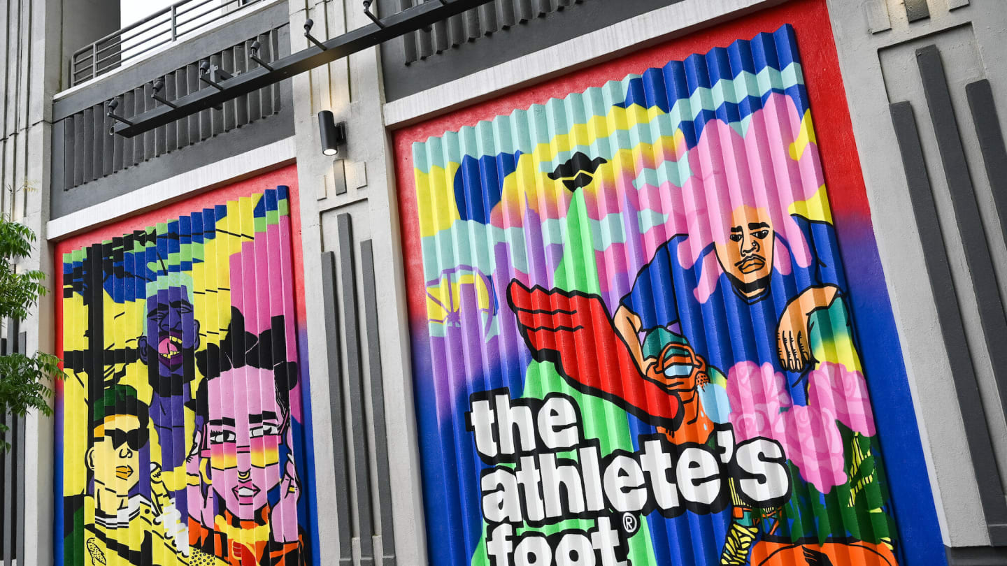 A bright mulitcolored mural featuring three faces on the side of a shipping container Bottom right is written The Athletes Foot
