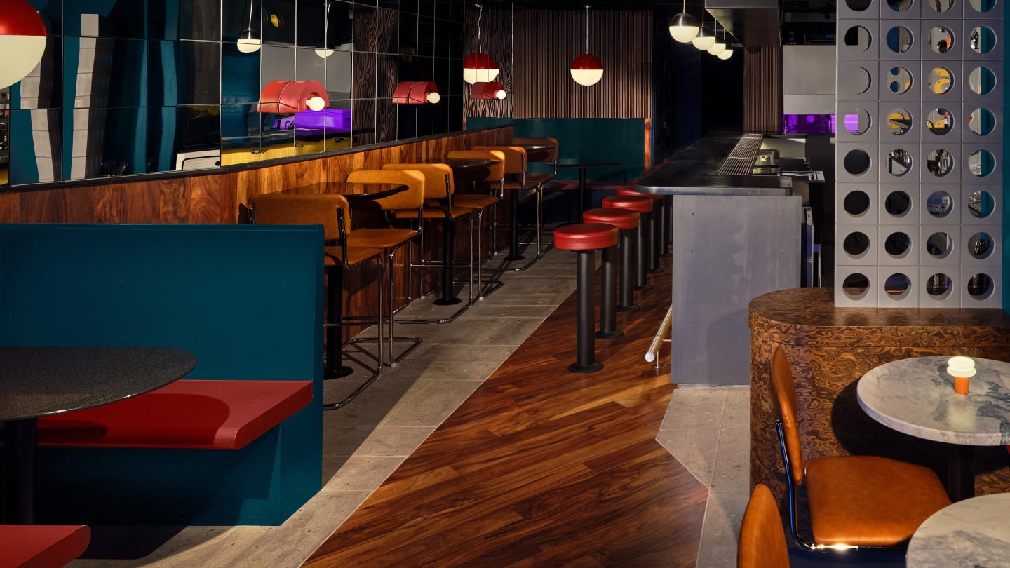 Dark retro bar interior with teal colored booths, wood paneling, circular tables and circular design cues throughout.