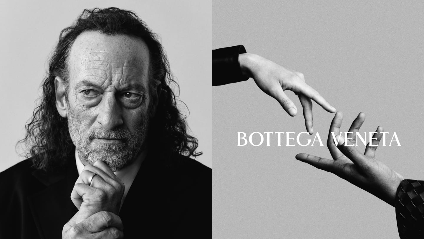 Black and white Bottega Veneta campaign image. On the left, an older man with long grey hair in a dark jacket, hands clasped. On the right, a close-up of a hand extending into frame.