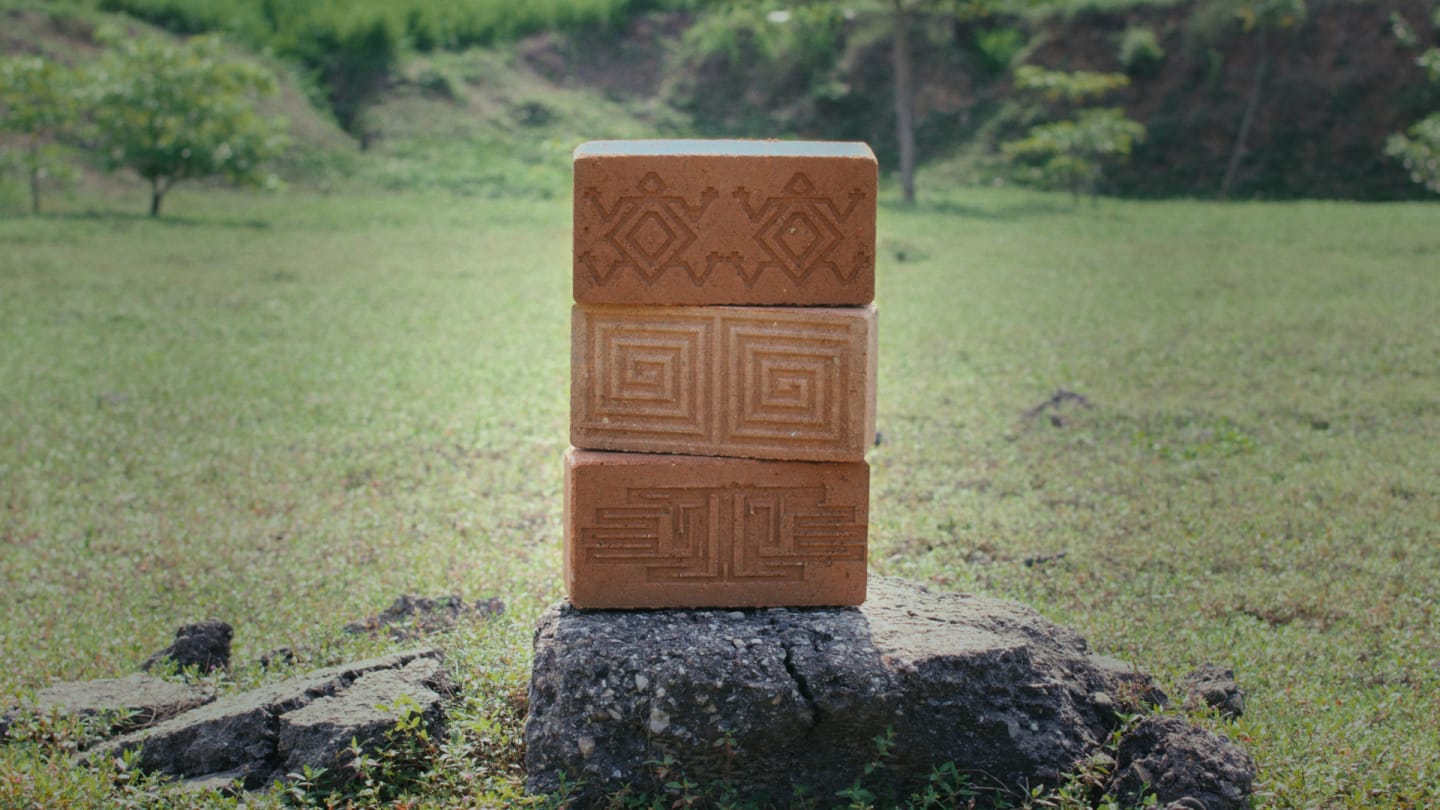 Three patterned bricks stacked on a rock in a grassy outdoor setting.