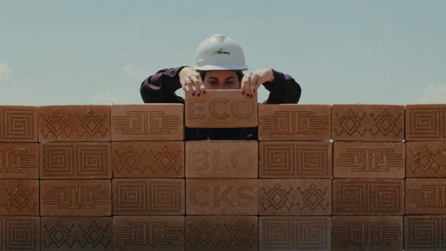 A worker in an Ecopetrol hard hat peers over a wall of patterned "ECO BLOCKS" against a clear sky.