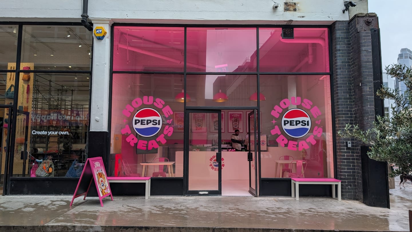 A storefront with pink-tinted windows featuring "House of Pepsi" logos on either side of the entrance on a rainy street.