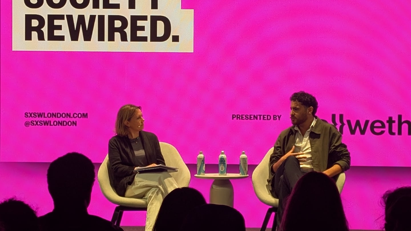 Man and woman on stage in front of a pink screen with the title Society Rewired.