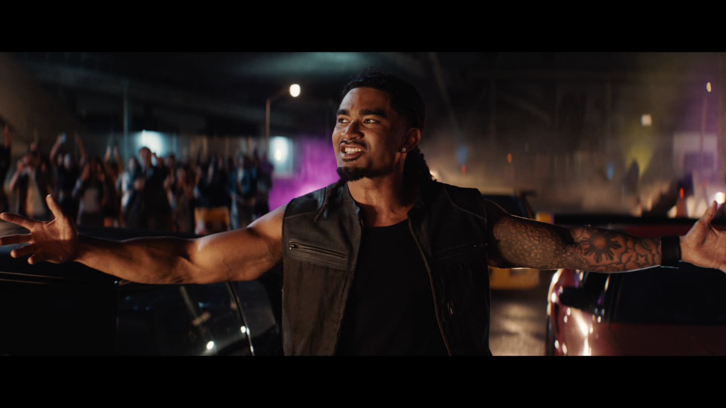 Image of a person standing in front of a street race with their arms spread wide, smiling.