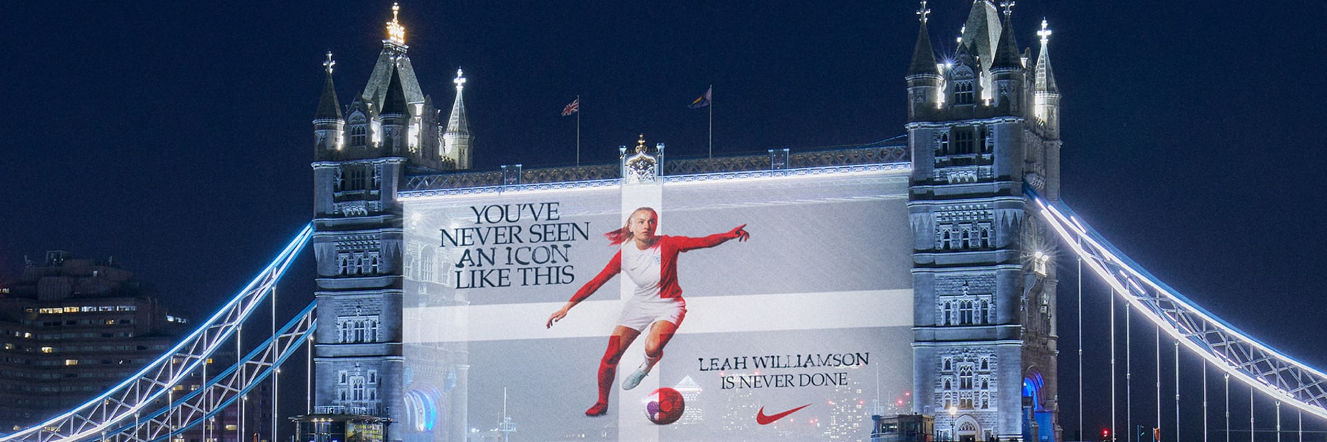 A projection onto London Tower Bridge at night-time. The projection shows a woman playing football accompanied by the words “YOU’VE NEVER SEEN AN ICON LIKE THIS” and “LEAH WILLIAMS IS NEVER DONE” There is a Nike logo in the bottom righthand corner.