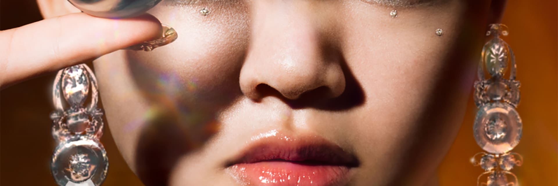 A close-up image of a woman with light skin and dark hair wearing silver glittered eyeshadow holds a silver ball.