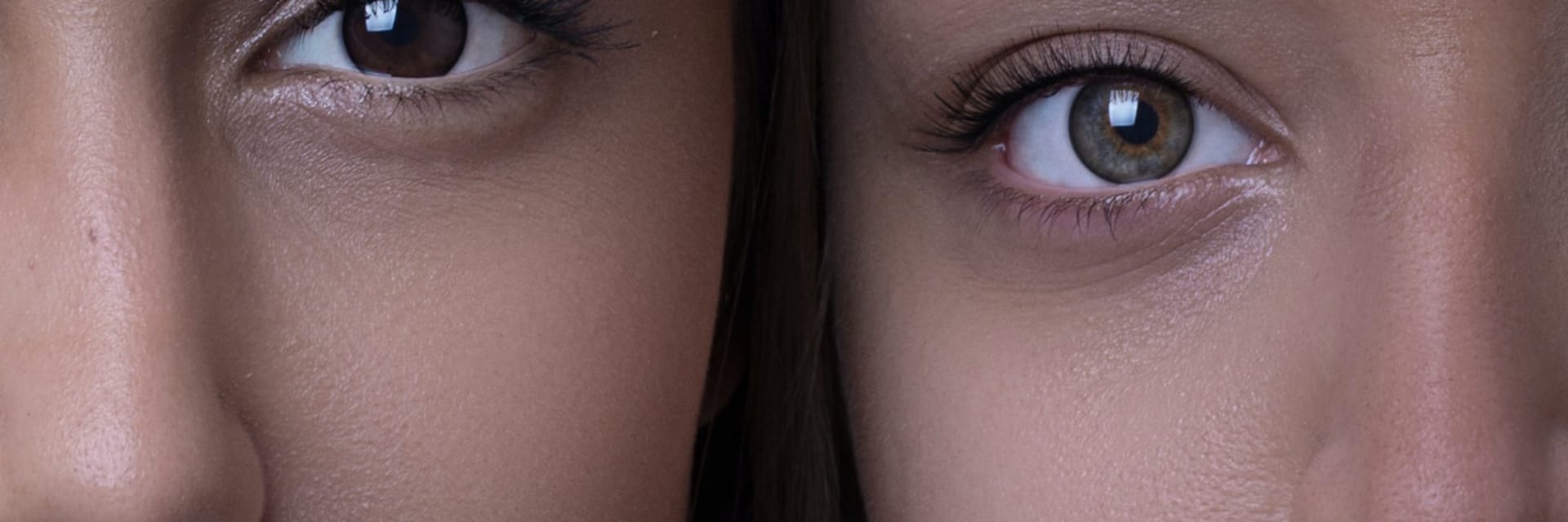 A close-up image of two women looking into the camera. On the left, a woman with tan skin, dark brown hair and dark brown eyes. On the right, a woman with light skin, brown hair and blue-green eyes.