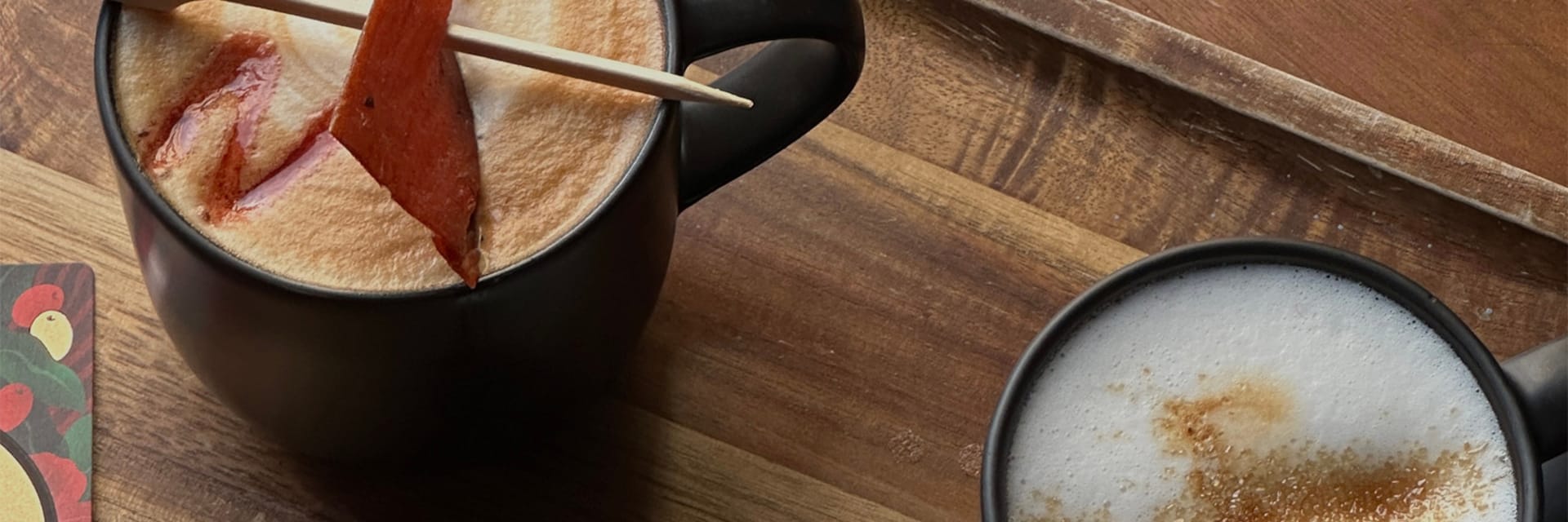 Two coffee cups on a wooden board one garnished with a slice of pork