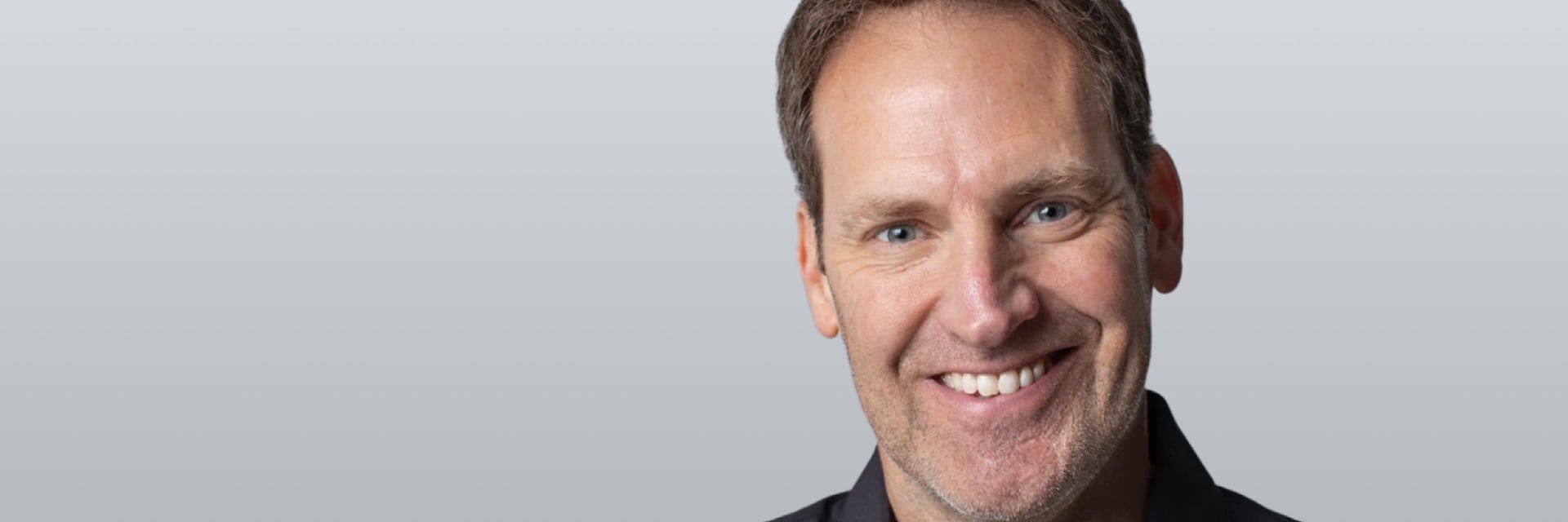 Jon Cook smiling wearing a gray button up shirt.