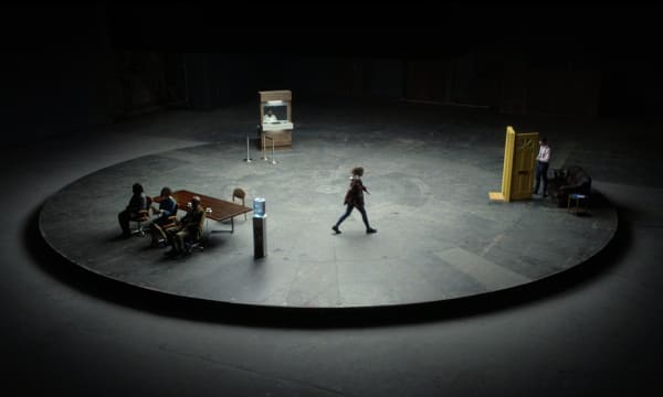 Raised circular platform featuring set of an office, front door, and bank teller with someone walking between the three to demonstrate 'vicious circle' effect