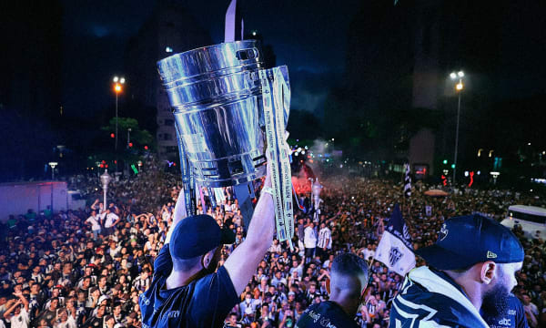 Person in black cap holding up big trophy with ribbons in it in front of large crowd