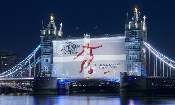 A projection onto London Tower Bridge at night-time. The projection shows a woman playing football accompanied by the words “YOU’VE NEVER SEEN AN ICON LIKE THIS” and “LEAH WILLIAMS IS NEVER DONE” There is a Nike logo in the bottom righthand corner.