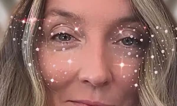 A blonde woman stares into the camera, only her eyes and nose showing, with a digital overlay of stars and sparkles accenting her eyes.