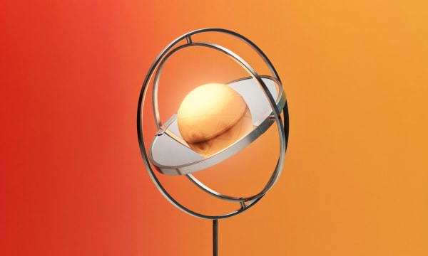 A spherical light bulb rests centered between two rotating circular rings. The light fixture sits in front of an orange-to-yellow backdrop.