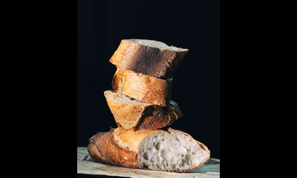 Four slices of baguette, cut diagonally, are stacked on top of each other in front of a black backdrop.